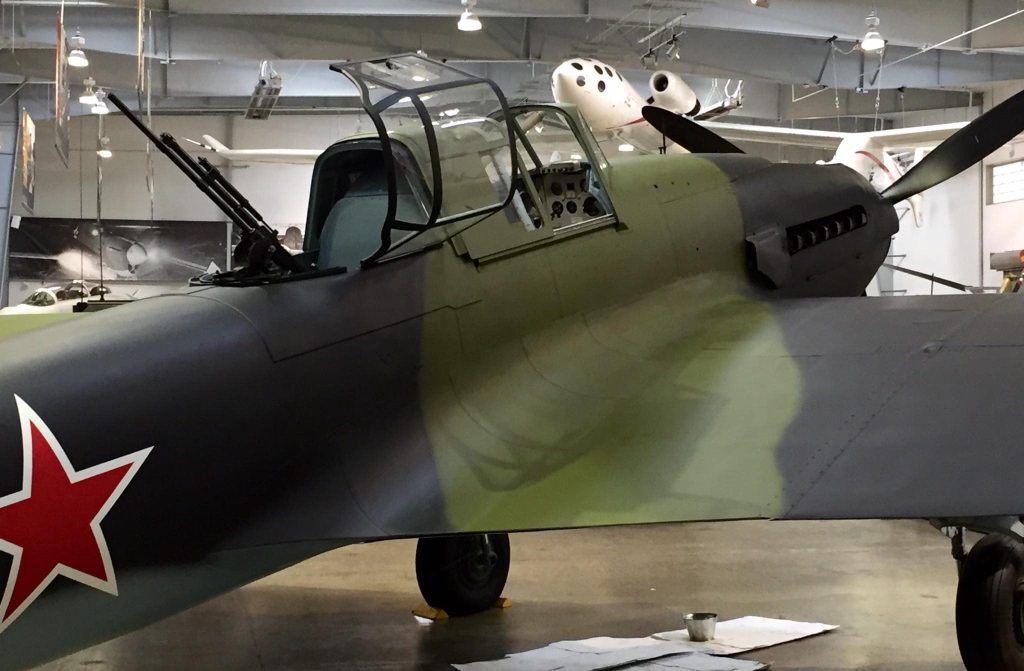 Close side view of Ilyushin Il-2 cockpit and rear machine gun in a museum hall.