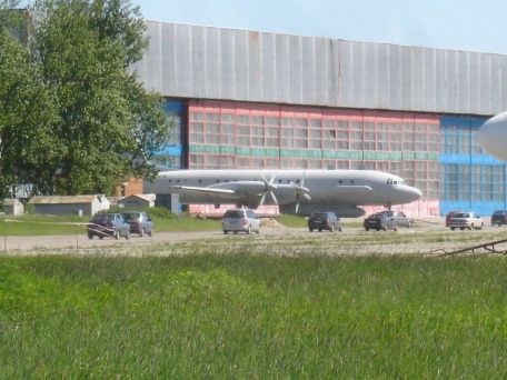 Grey Ilyushin Il-20 parked near a large hangar with vehicles nearby.