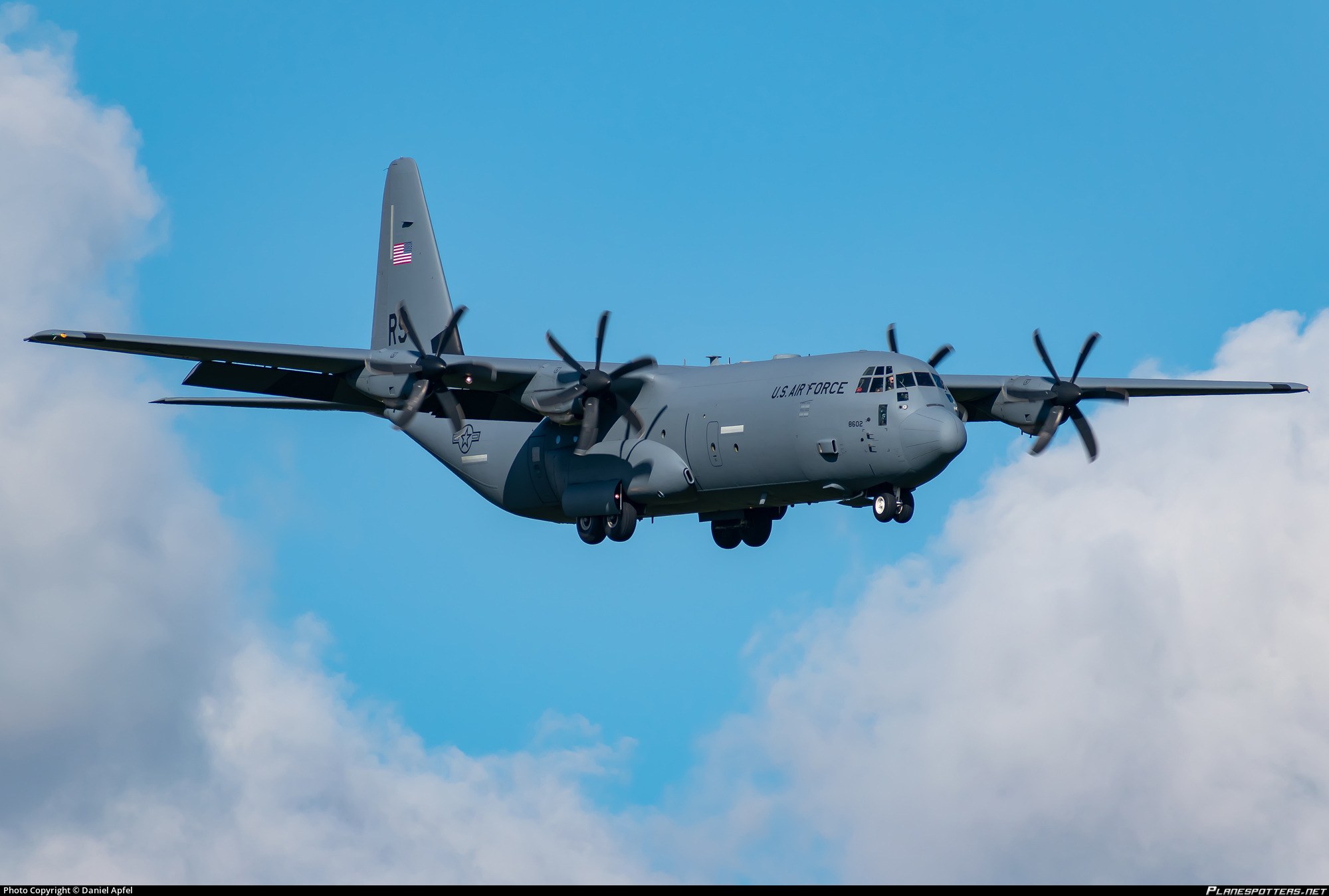 Grey U.S. Air Force Lockheed C-130 Hercules flying with landing gear partly extended.