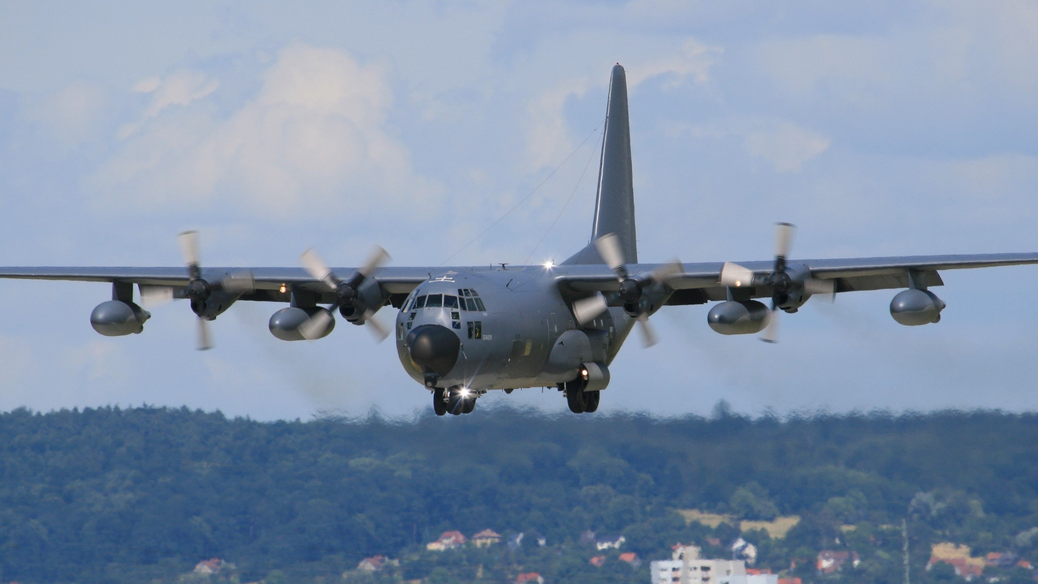 Grey Lockheed C-130 Hercules approaching head-on with landing gear down.