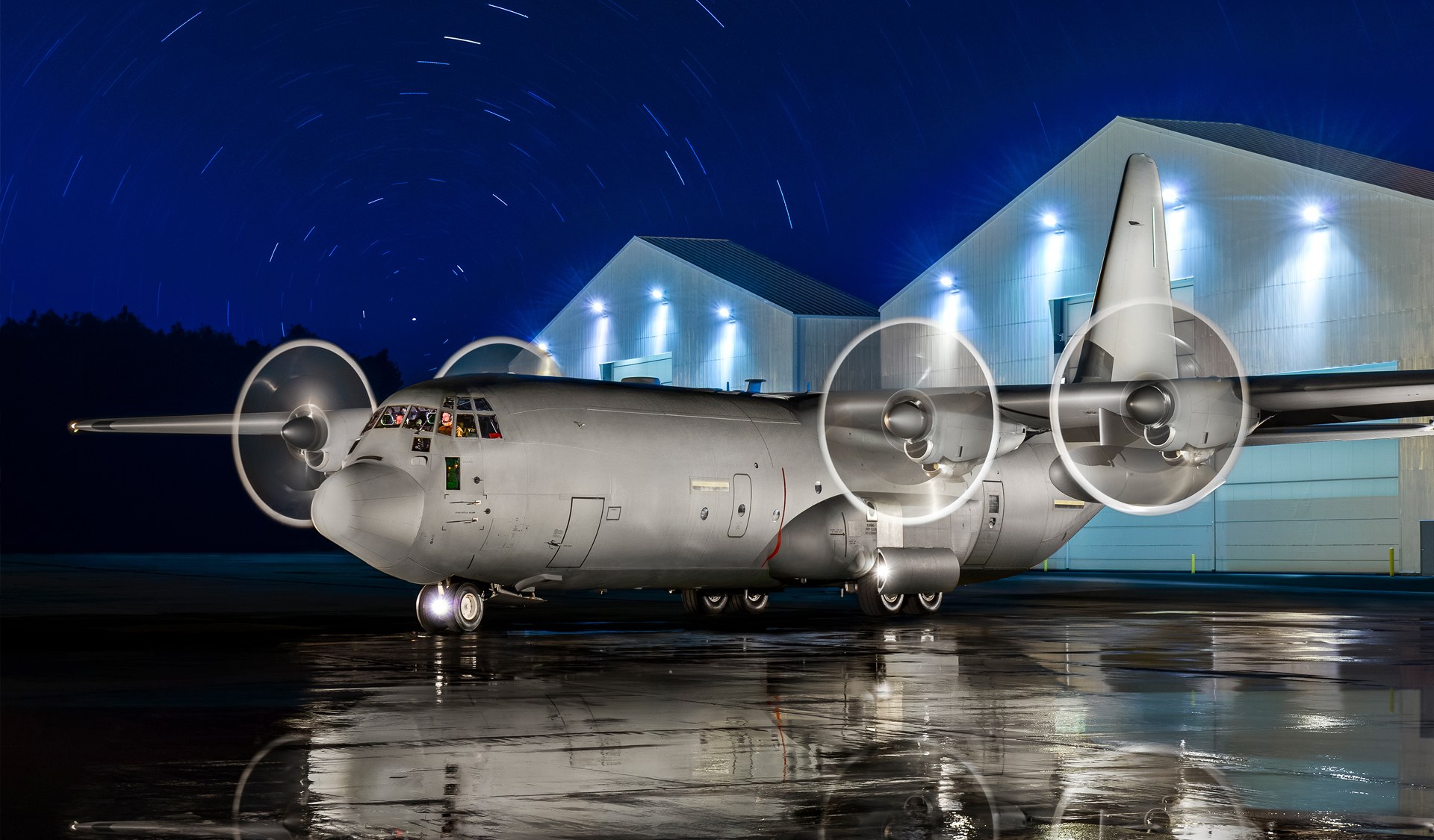 Grey Lockheed C-130 Hercules landing with propellers blurred and gear down.