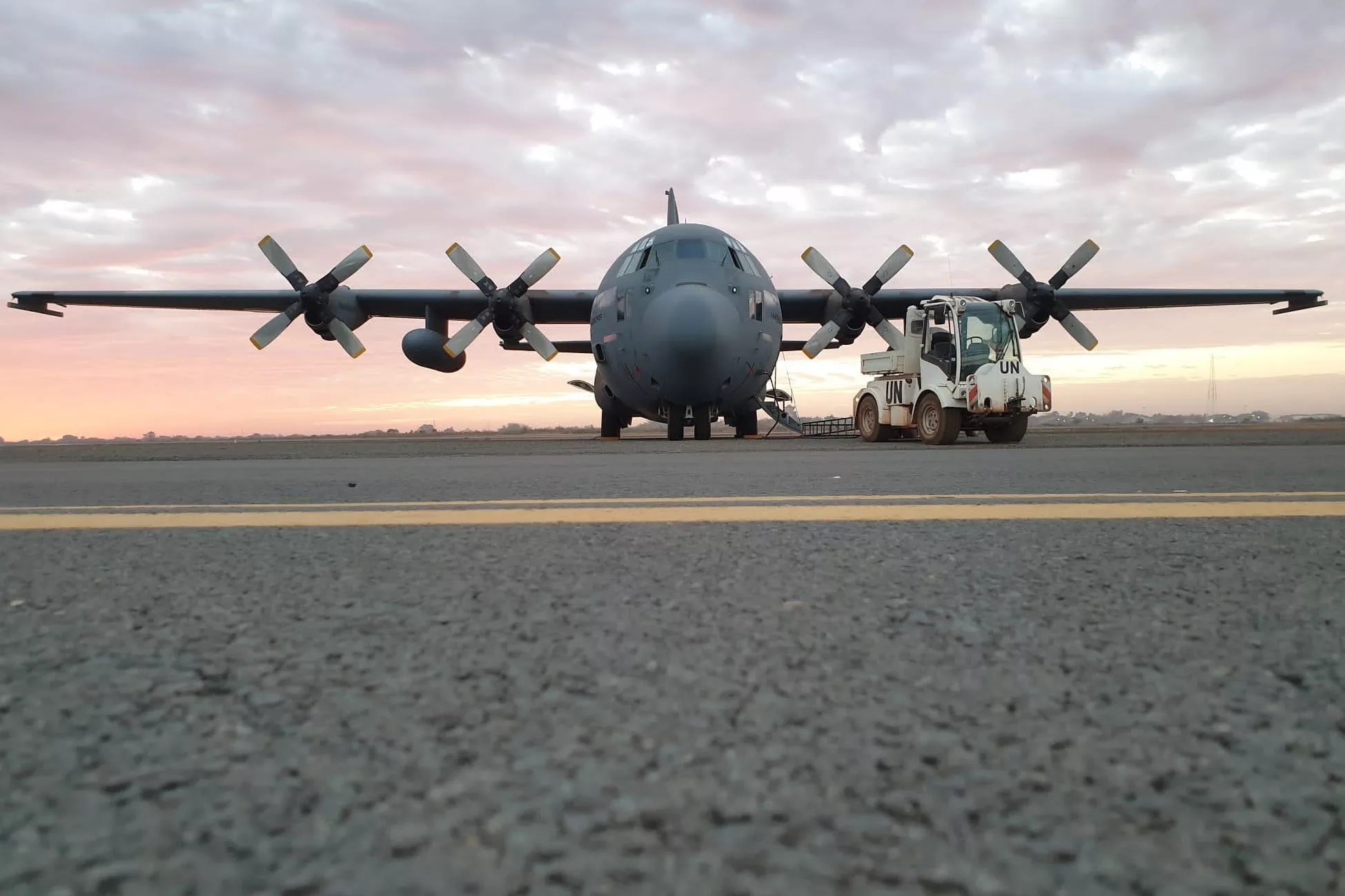 Lockheed C-130 Hercules parked at night with spinning propellers and wet ramp reflections.