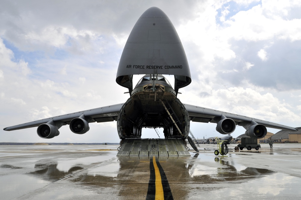 Air Force Reserve Command C-5 Galaxy with open nose and cargo ramp on wet pavement.