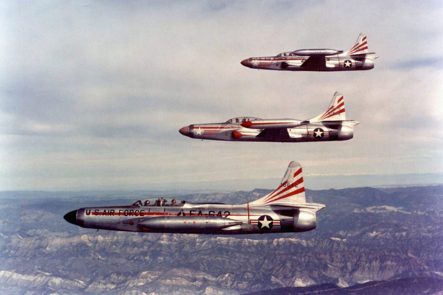 Three F-94 Starfires flying in formation over mountains.