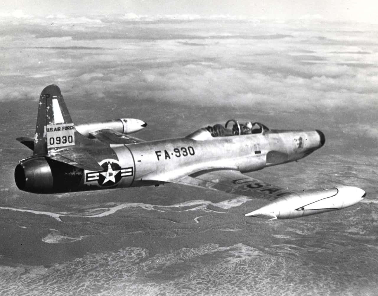 Black-and-white view of F-94 Starfire FA-930 flying over terrain.