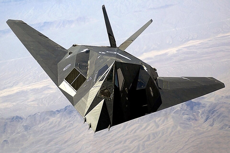 Lockheed F-117 Nighthawk in flight from the front quarter, showing the faceted stealth-aircraft shape and sharply angled wings.