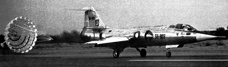 Lockheed F-104 Starfighter landing with a drag chute deployed, showing the needle-nose fuselage and short straight wings of the supersonic interceptor.