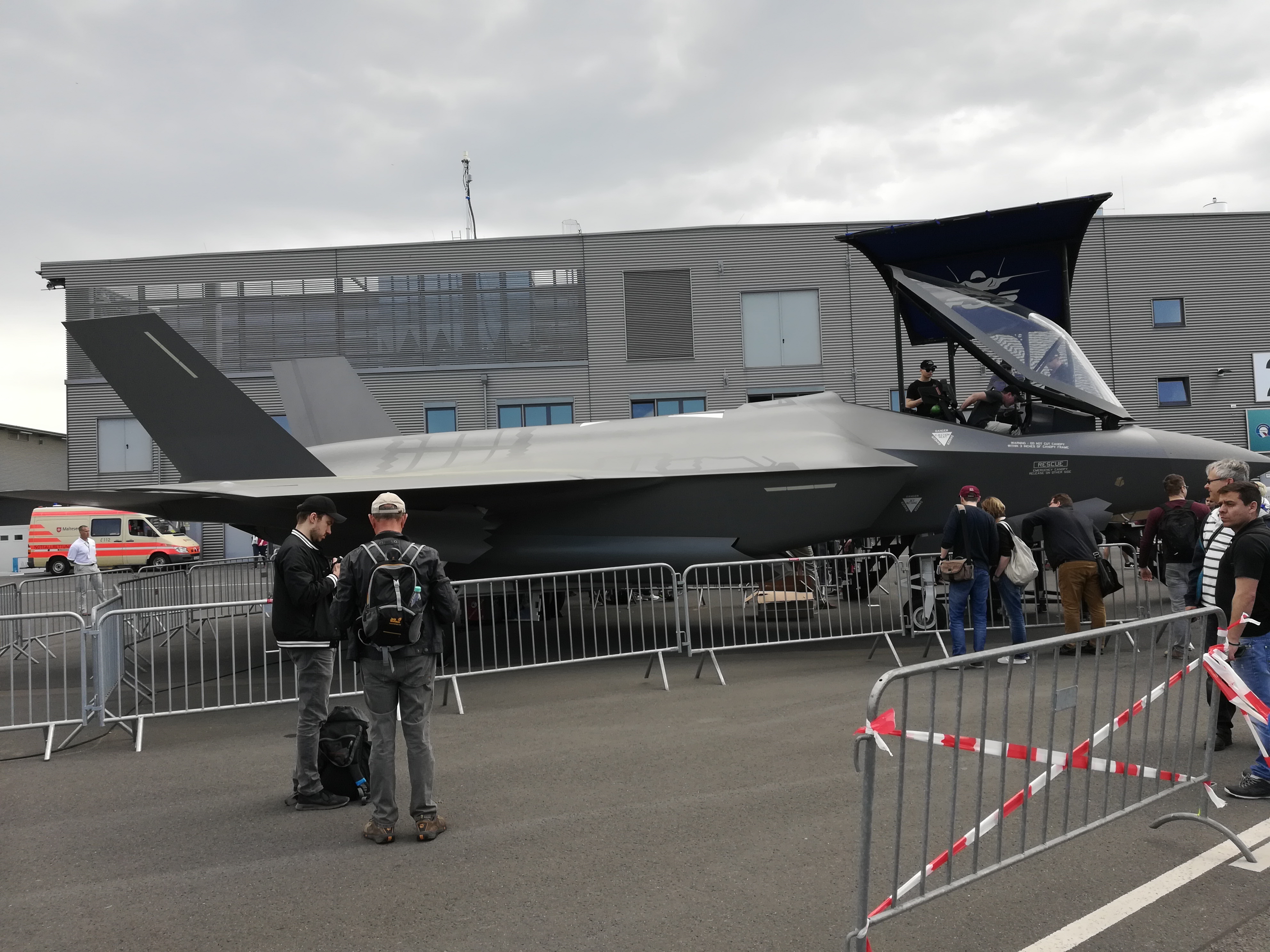 Lockheed Martin F-35 Lightning II parked on display with spectators and barriers around it, showing the single-engine stealth fighter in a public exhibition setting.