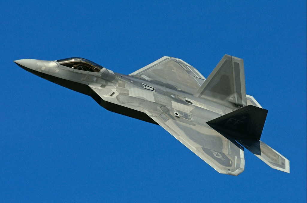 Grey F-22 Raptor banking left against a clear blue sky.