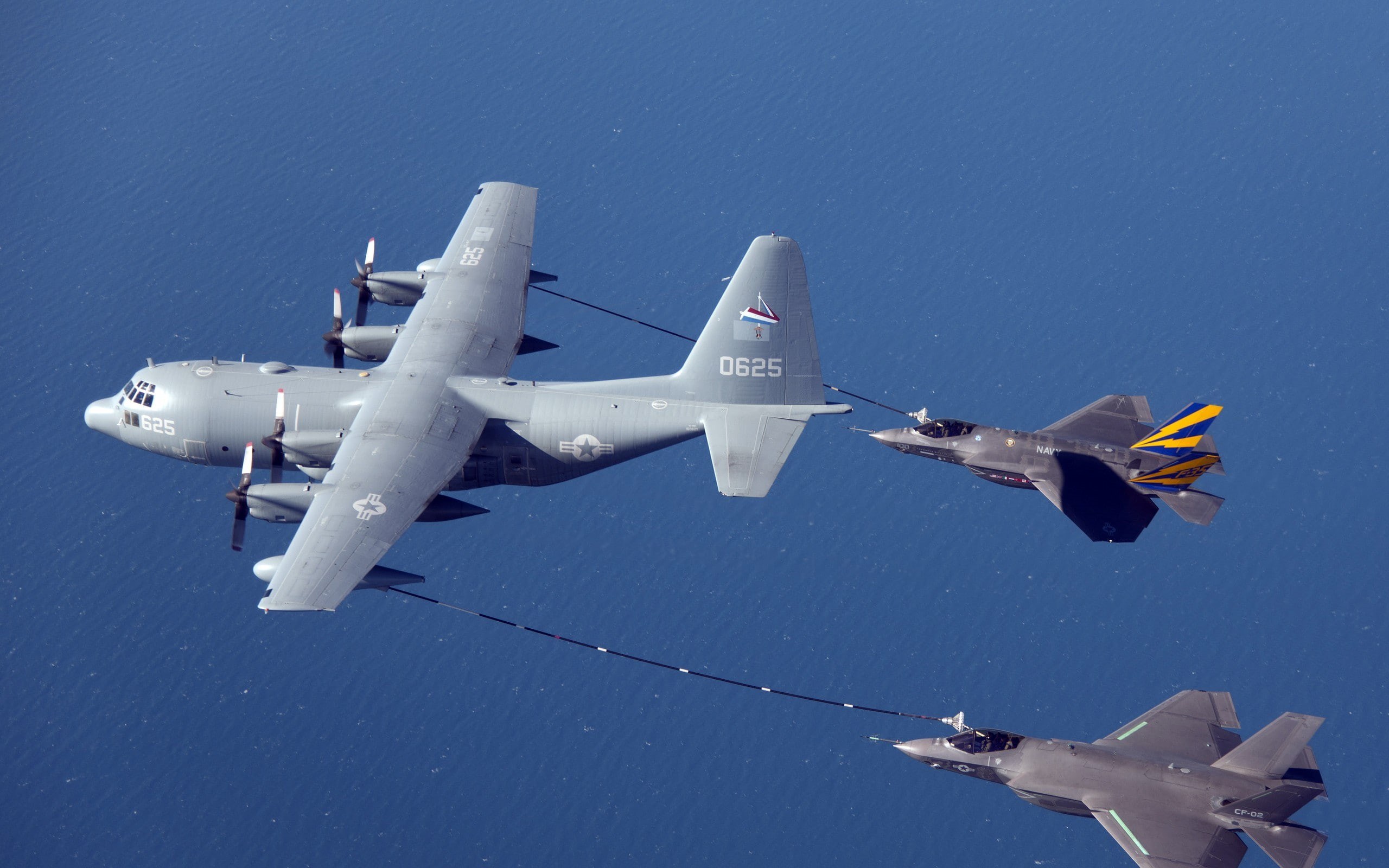 Two F-35 Lightning II aircraft flying near a KC-130 tanker over water.