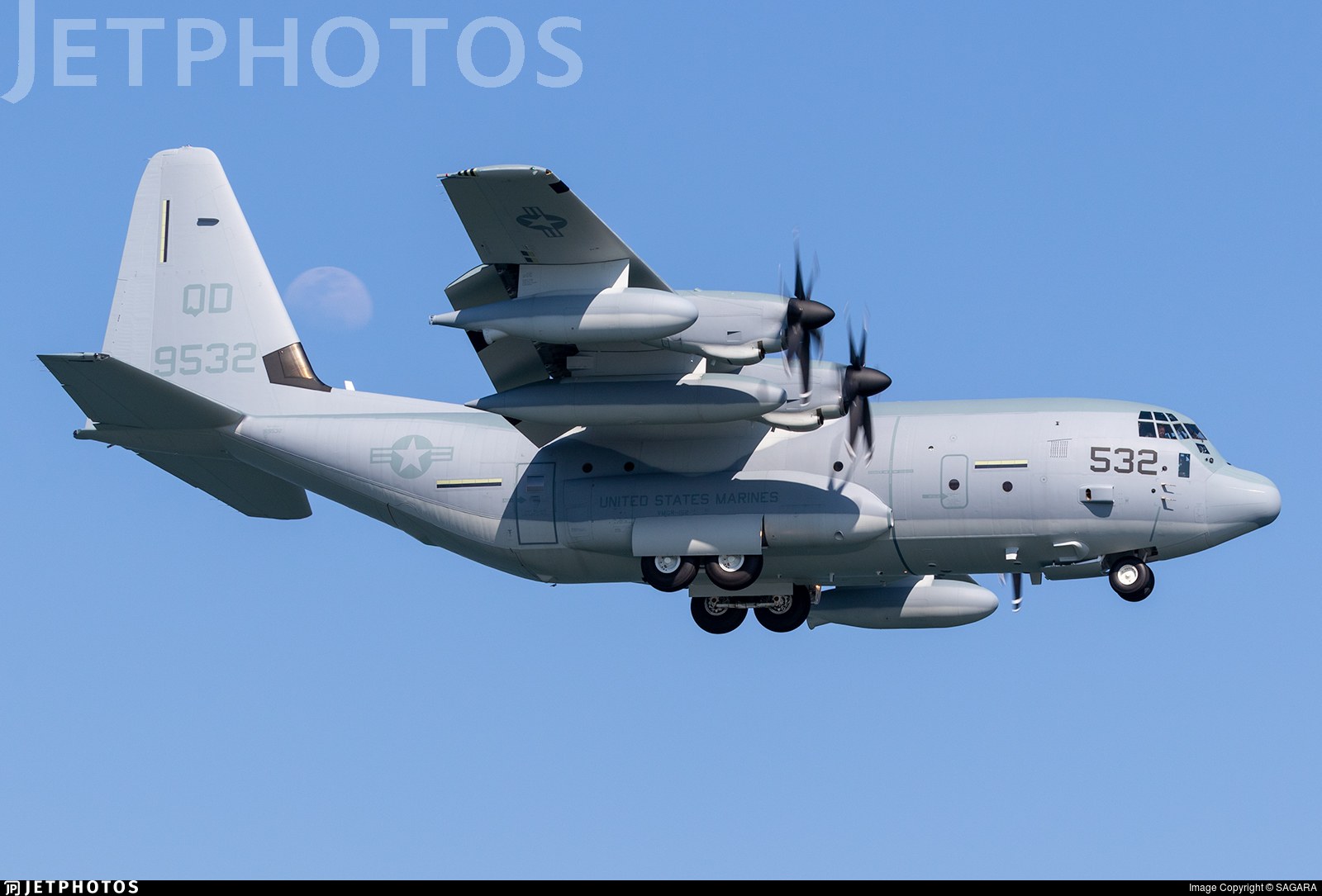 Marine KC-130J 532 flying with landing gear down and propellers turning.