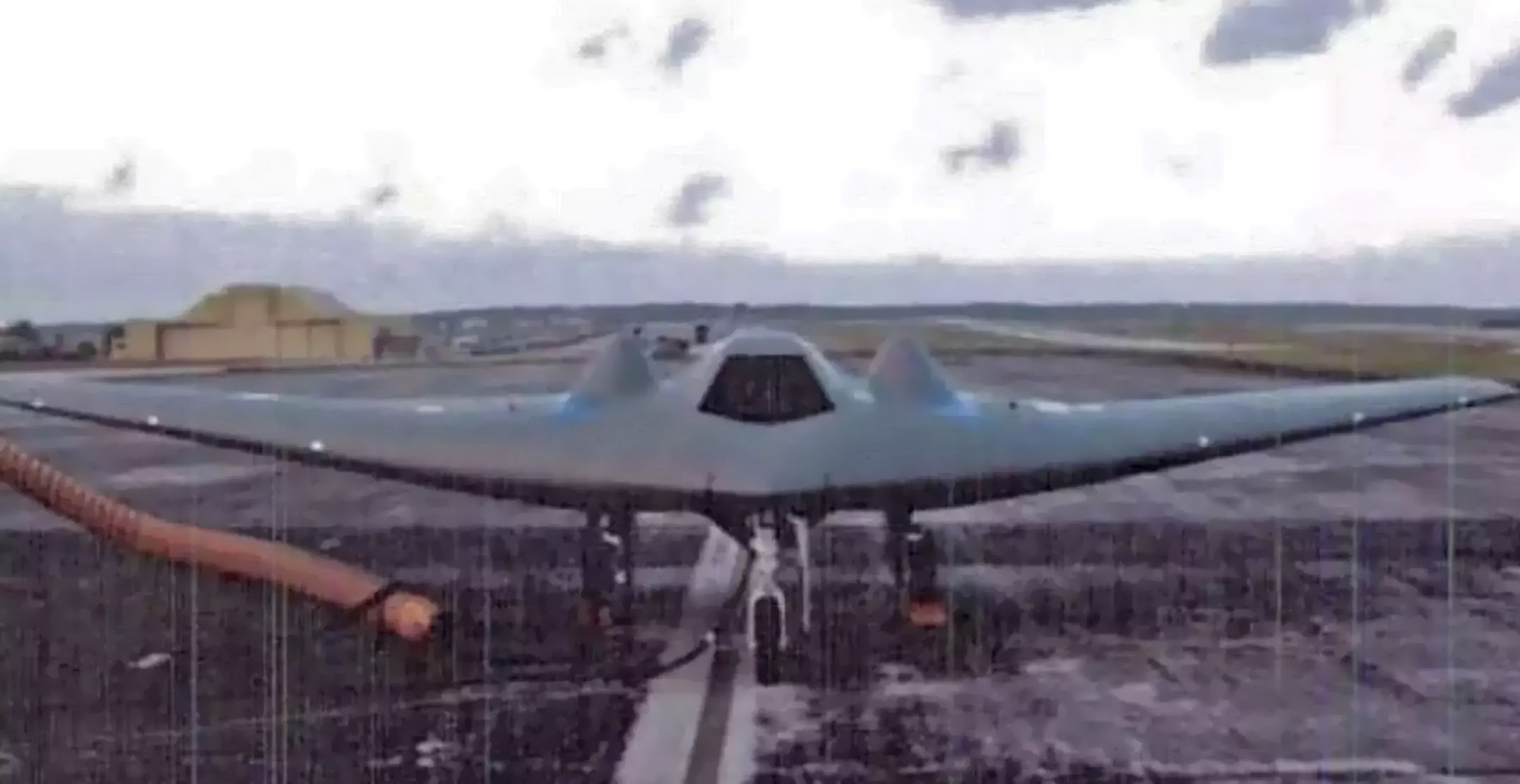 Low-resolution front view of an RQ-170 Sentinel on a ramp behind a fence.