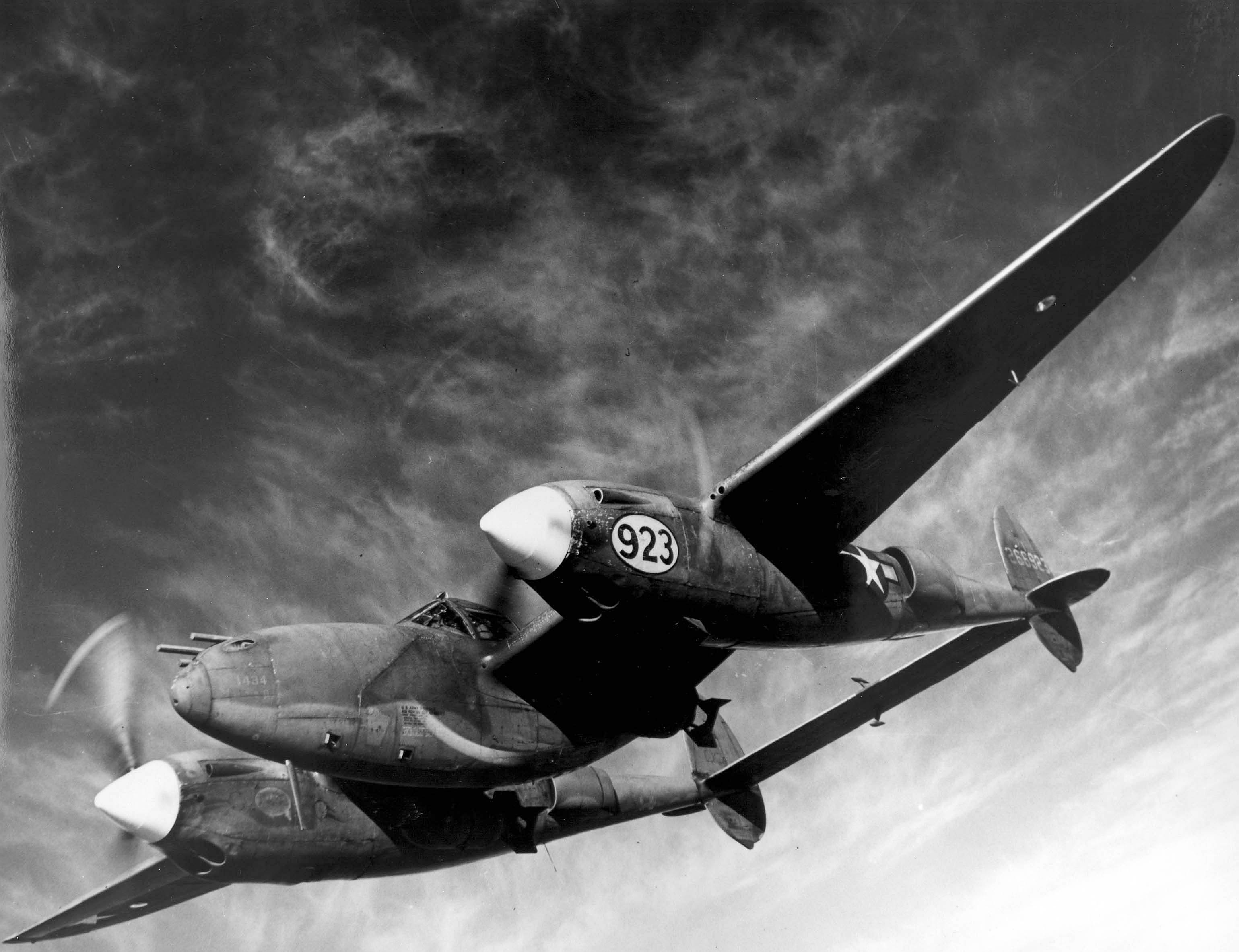 Lockheed P-38 Lightning fighter-bomber in flight, showing the twin-boom layout, central cockpit nacelle, and twin engines that define the aircraft profile.