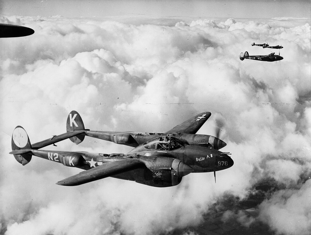 P-38 Lightning aircraft of the 364th Fighter Group flying in formation above clouds, showing Lockheed's twin-boom fighter in wartime service.