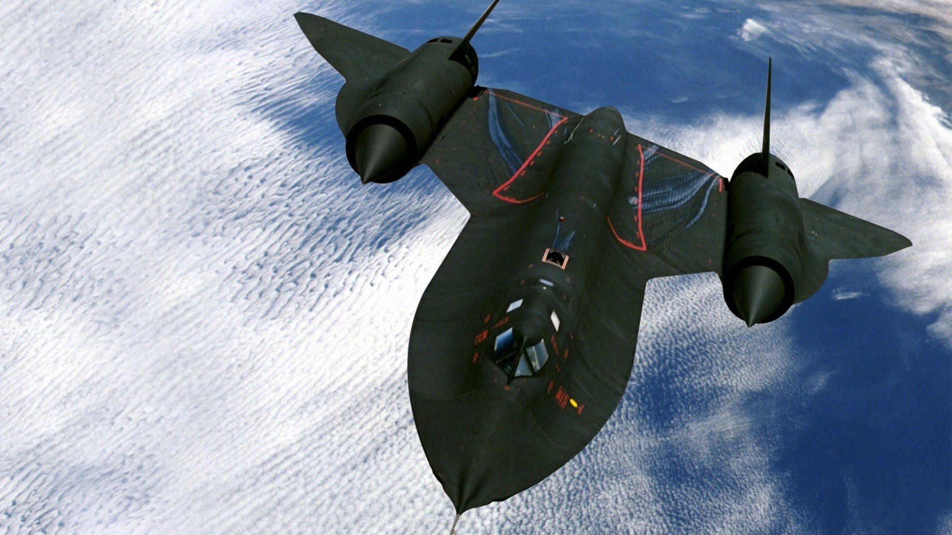 SR-71 Blackbird seen from above over clouds and blue water.
