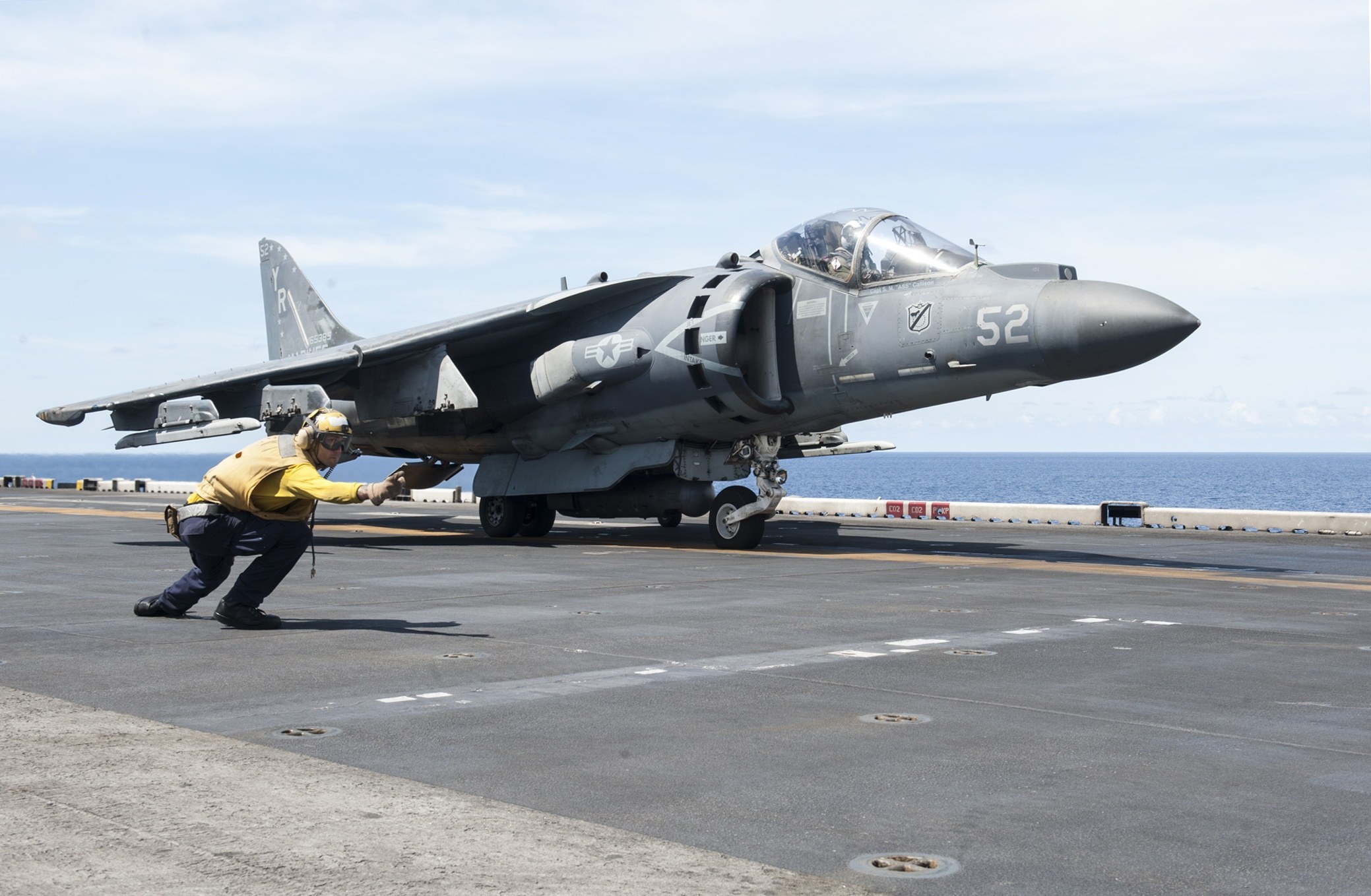 AV-8B Harrier II 52 on a carrier deck with a deck crew member in front.