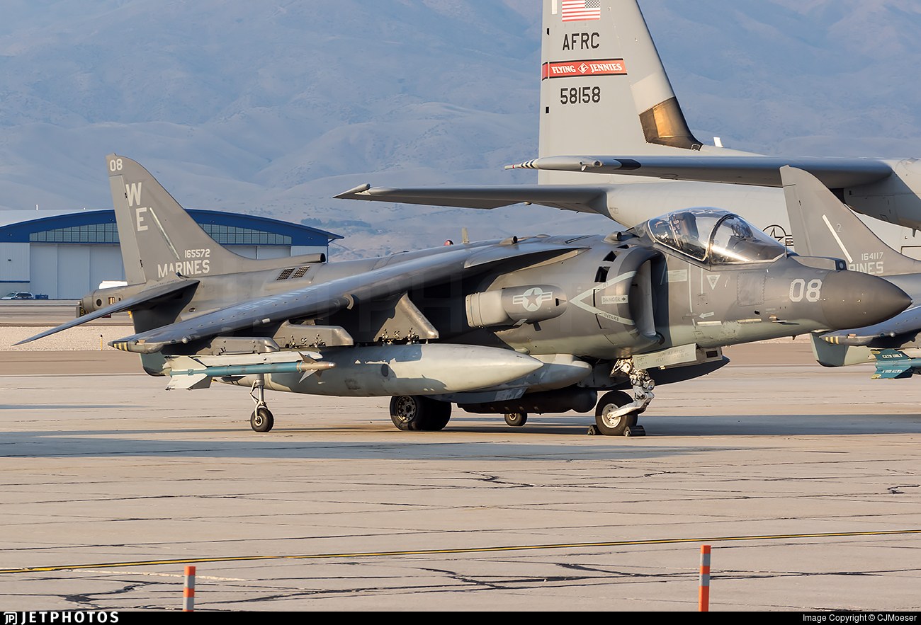 Marine AV-8B Harrier II 08 parked on a ramp with a C-130 tail behind it.