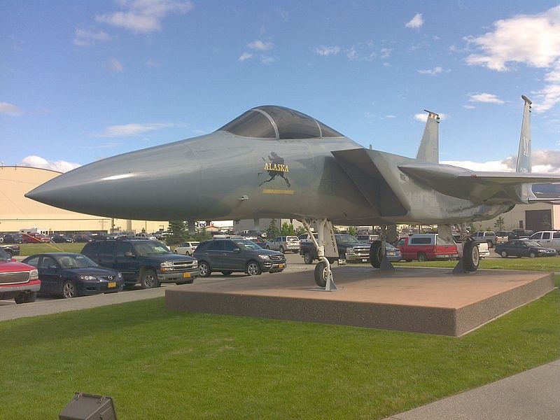 F-15 Eagle displayed on a pedestal beside parked cars.