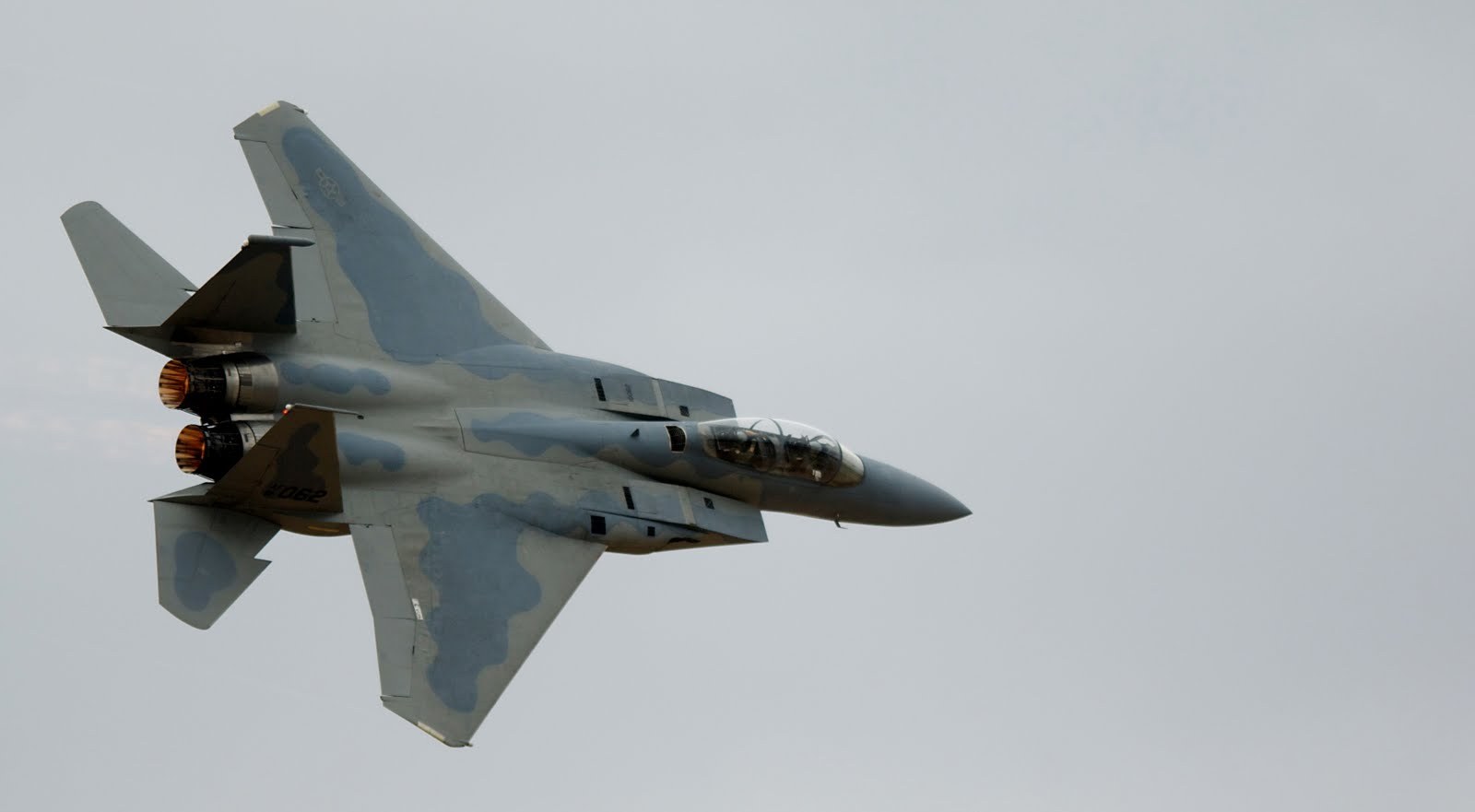 F-15 Eagle banking with underside and twin engine exhausts visible.
