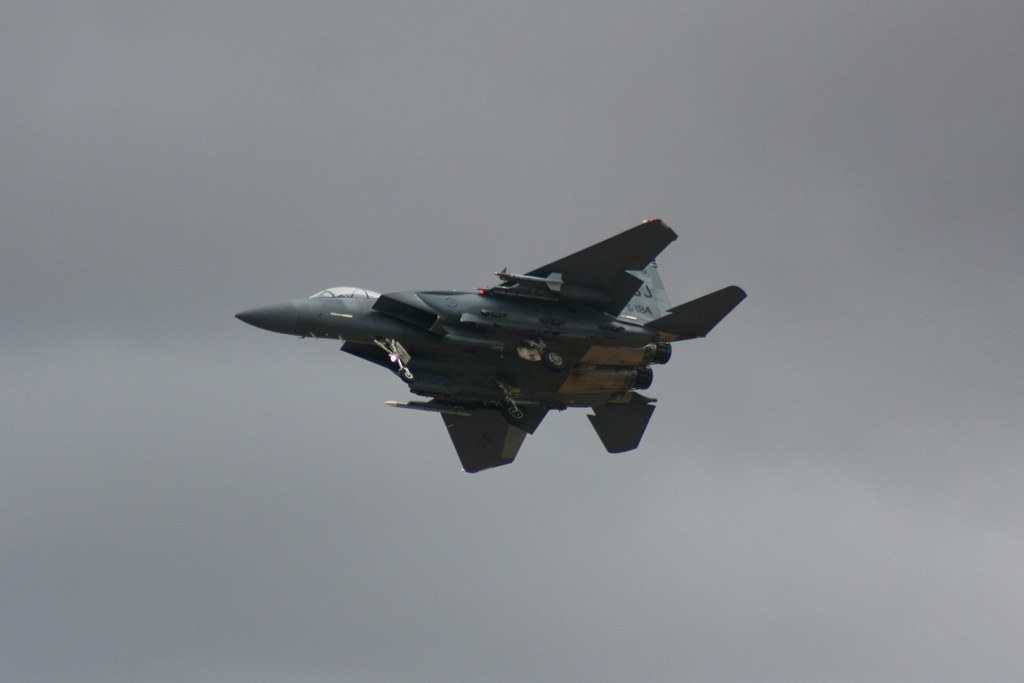 Dark gray F-15E Strike Eagle flying against an overcast sky with external stores under the wings.
