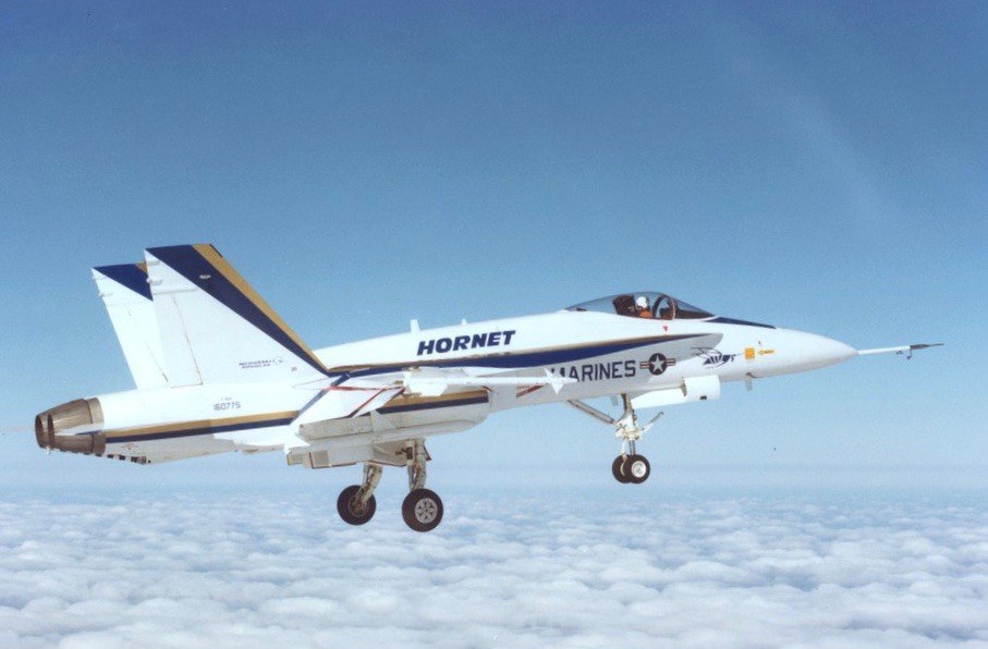 White F/A-18 Hornet prototype in Marines markings flying with landing gear down.