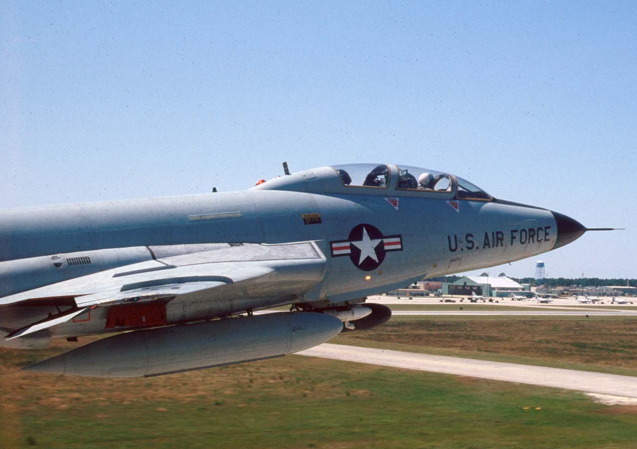 U.S. Air Force F-101 Voodoo shown close from the side in flight over an airfield.