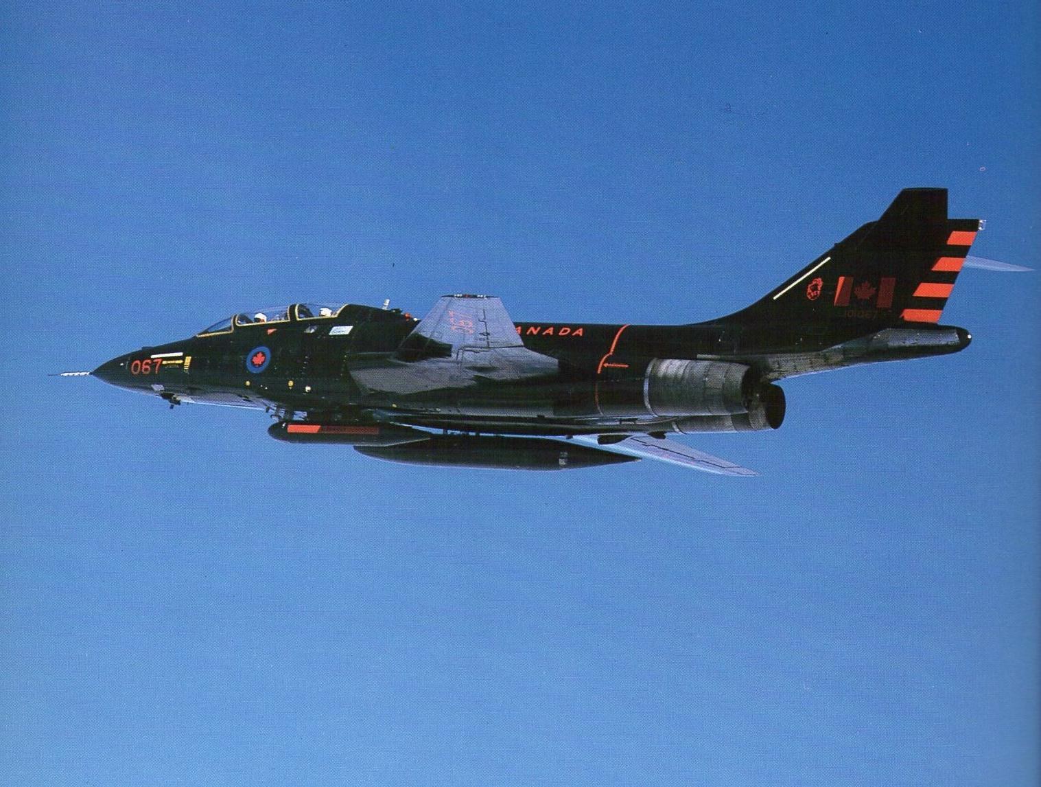 Dark Canadian-marked F-101 Voodoo flying against a clear blue sky.