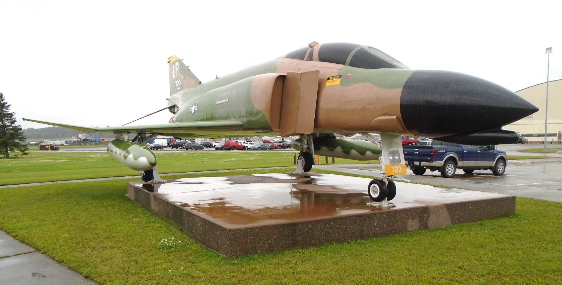 Camouflaged F-4 Phantom II displayed on a low outdoor pedestal with landing gear extended.