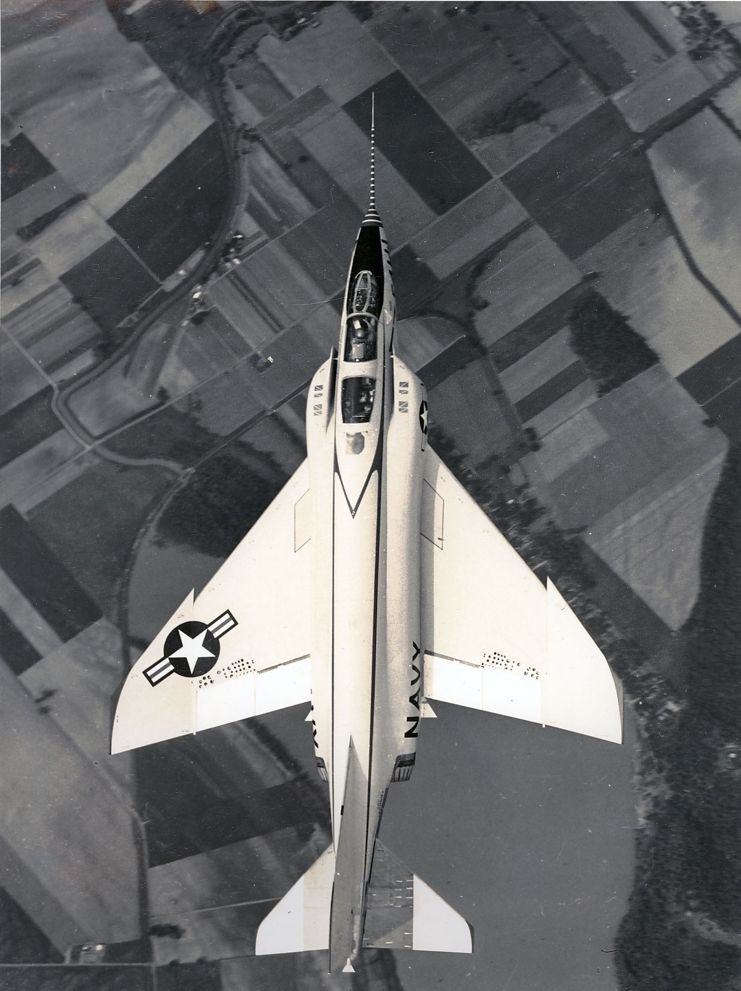 Black-and-white top-down view of an F-4 Phantom II flying above farmland.