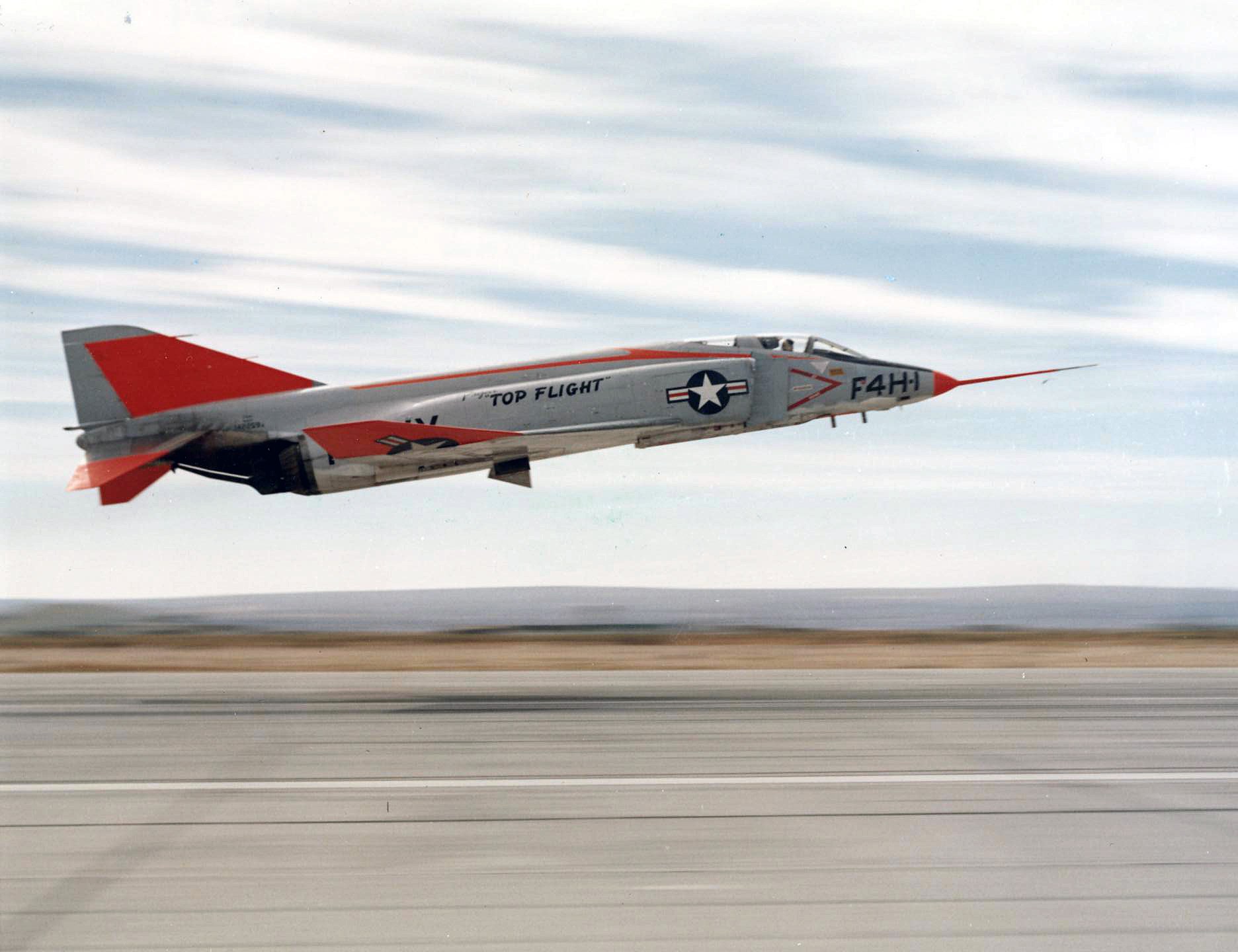 White and red F4H-1 Phantom marked Top Flight making a low pass over a runway.