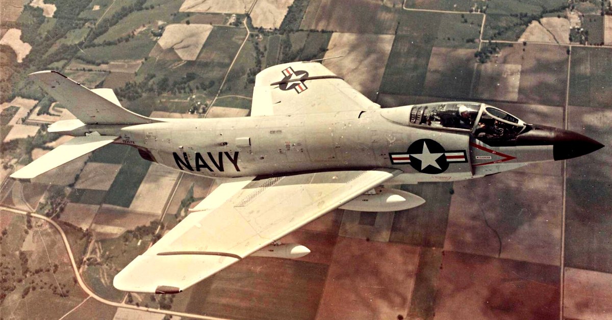 U.S. Navy F3H Demon flying above patchwork farmland with gear retracted.
