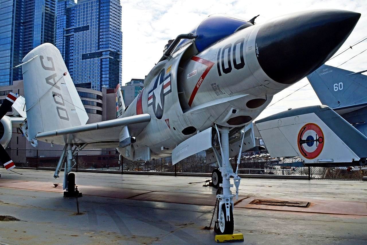 F3H Demon numbered 100 displayed outdoors near buildings with landing gear down.