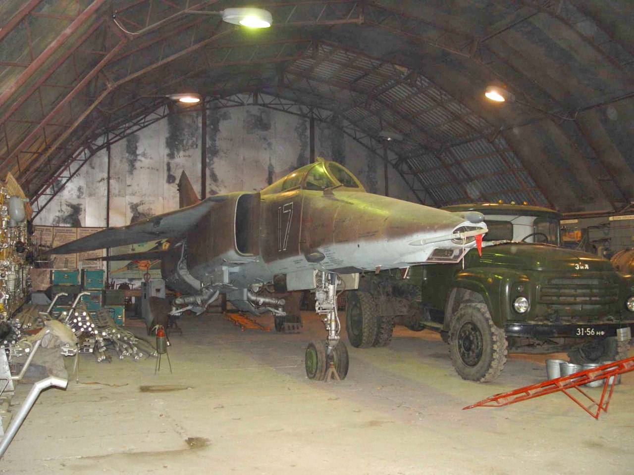 Camouflaged MiG-27 parked inside a hangar beside a military truck.