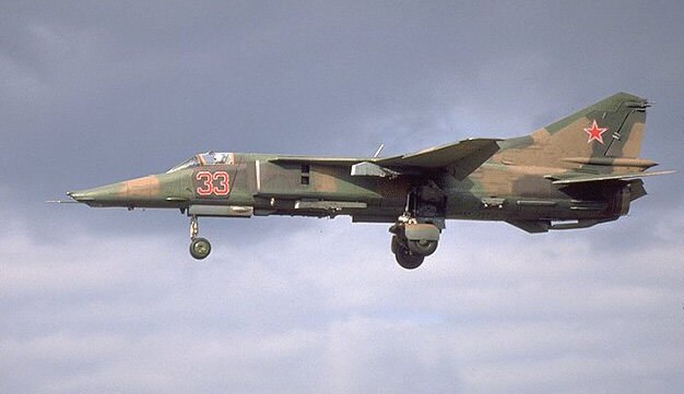 Camouflaged MiG-27 numbered 33 flying with landing gear extended and red star tail marking.