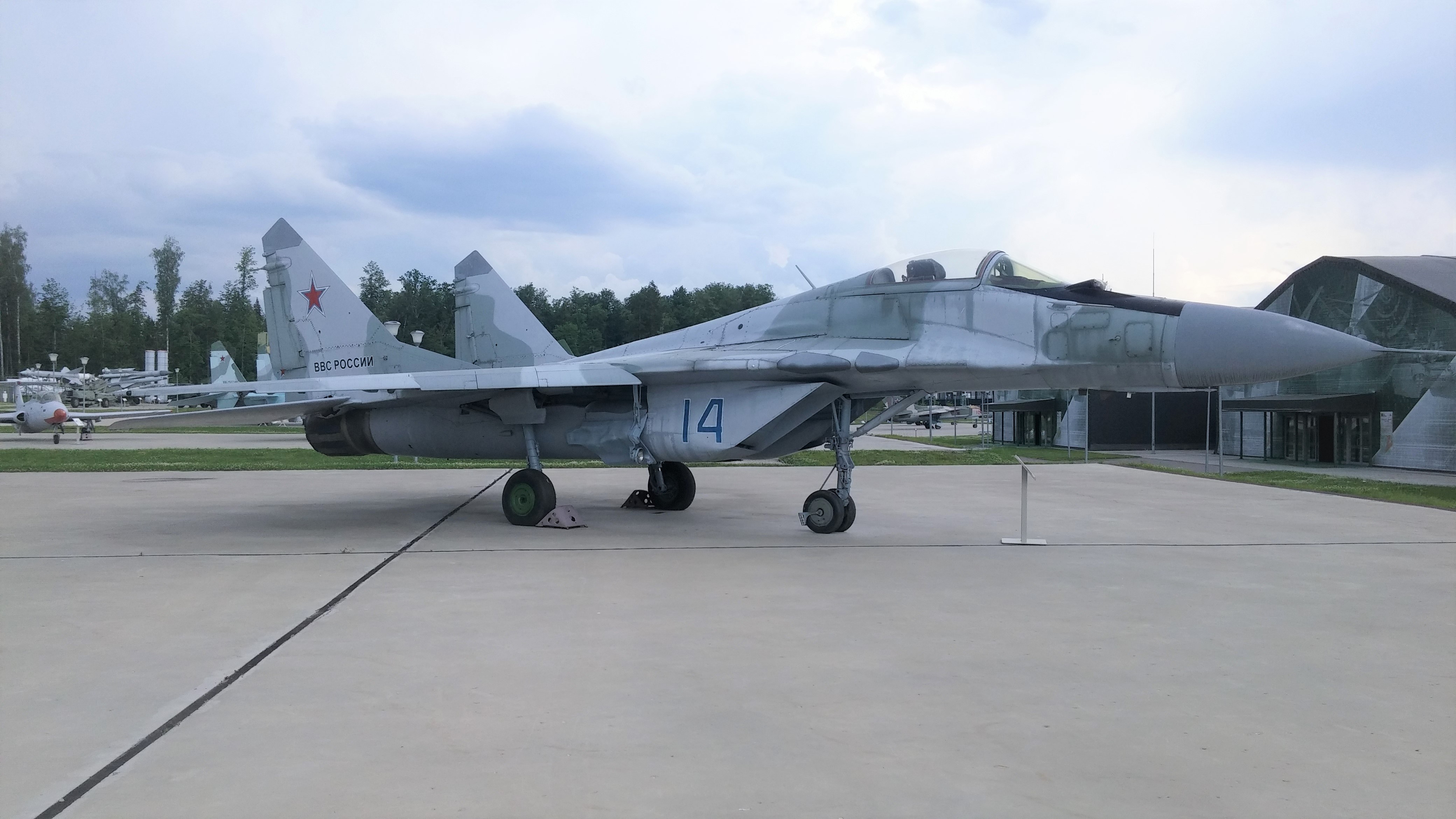 Light gray MiG-29 numbered 14 displayed on a concrete pad with red star tail markings.