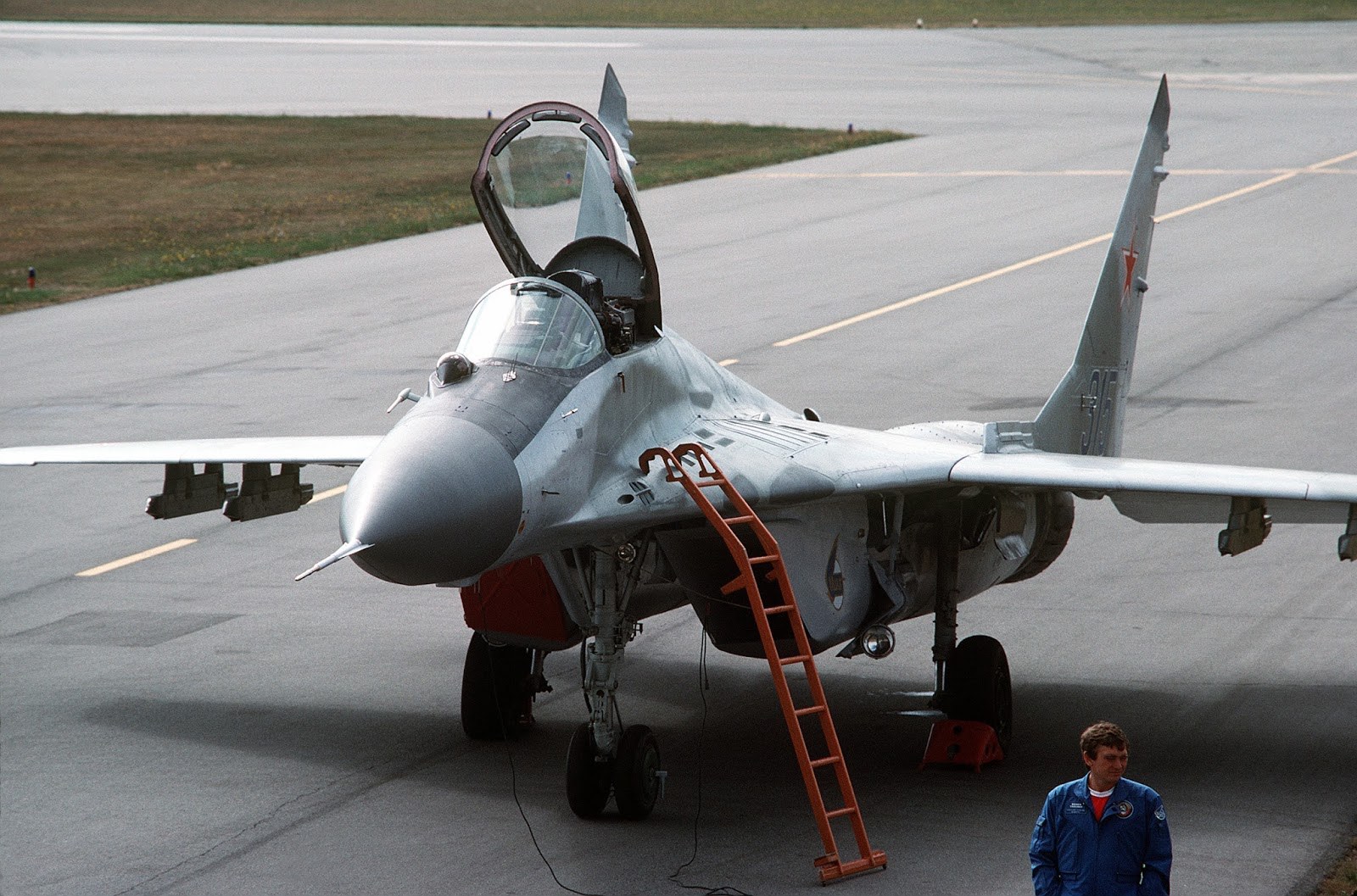 MiG-29 parked on a ramp with canopy open and an orange ladder at the cockpit.