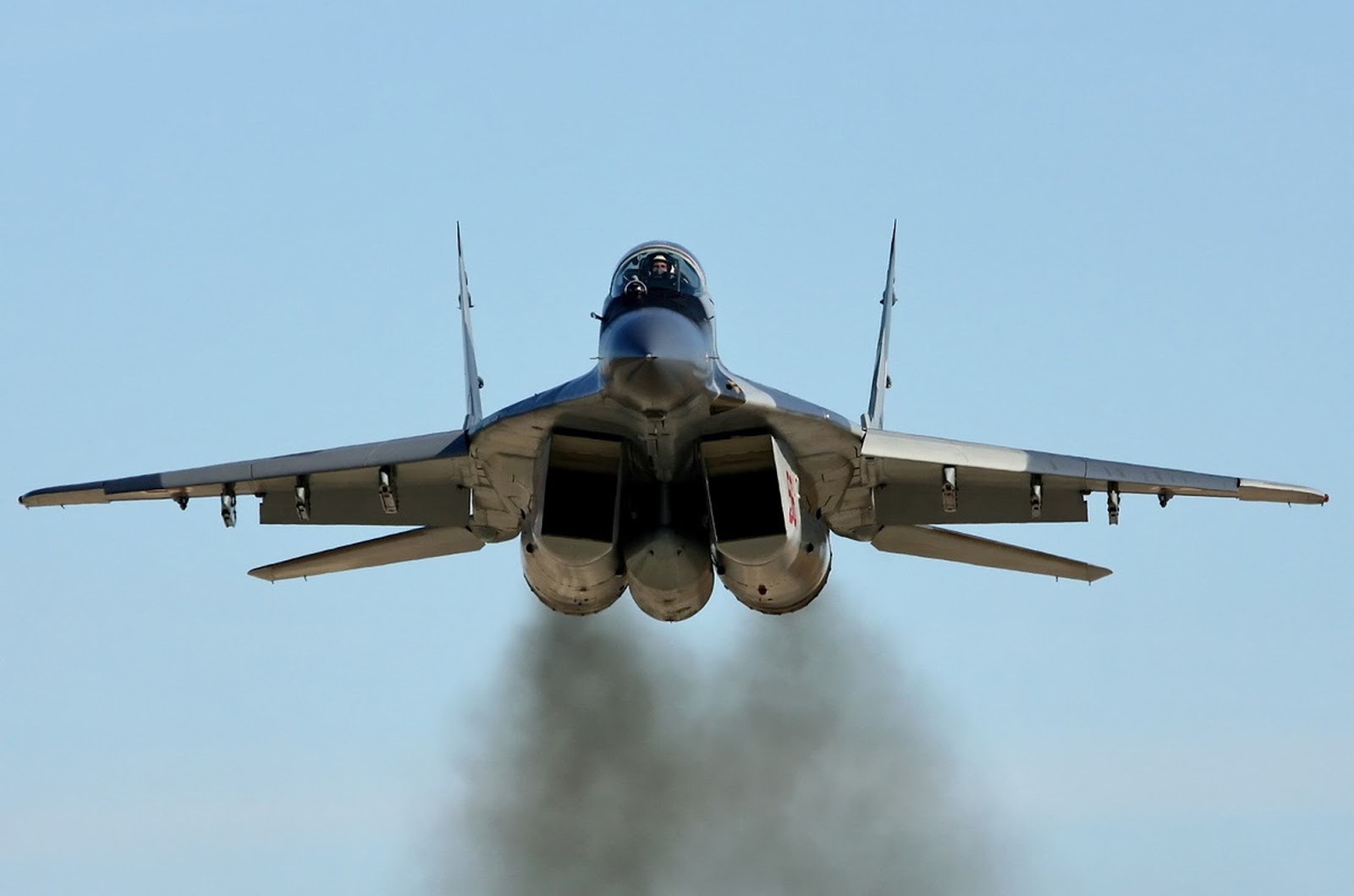 Rear view of a MiG-29 climbing with exhaust smoke below the twin engines.