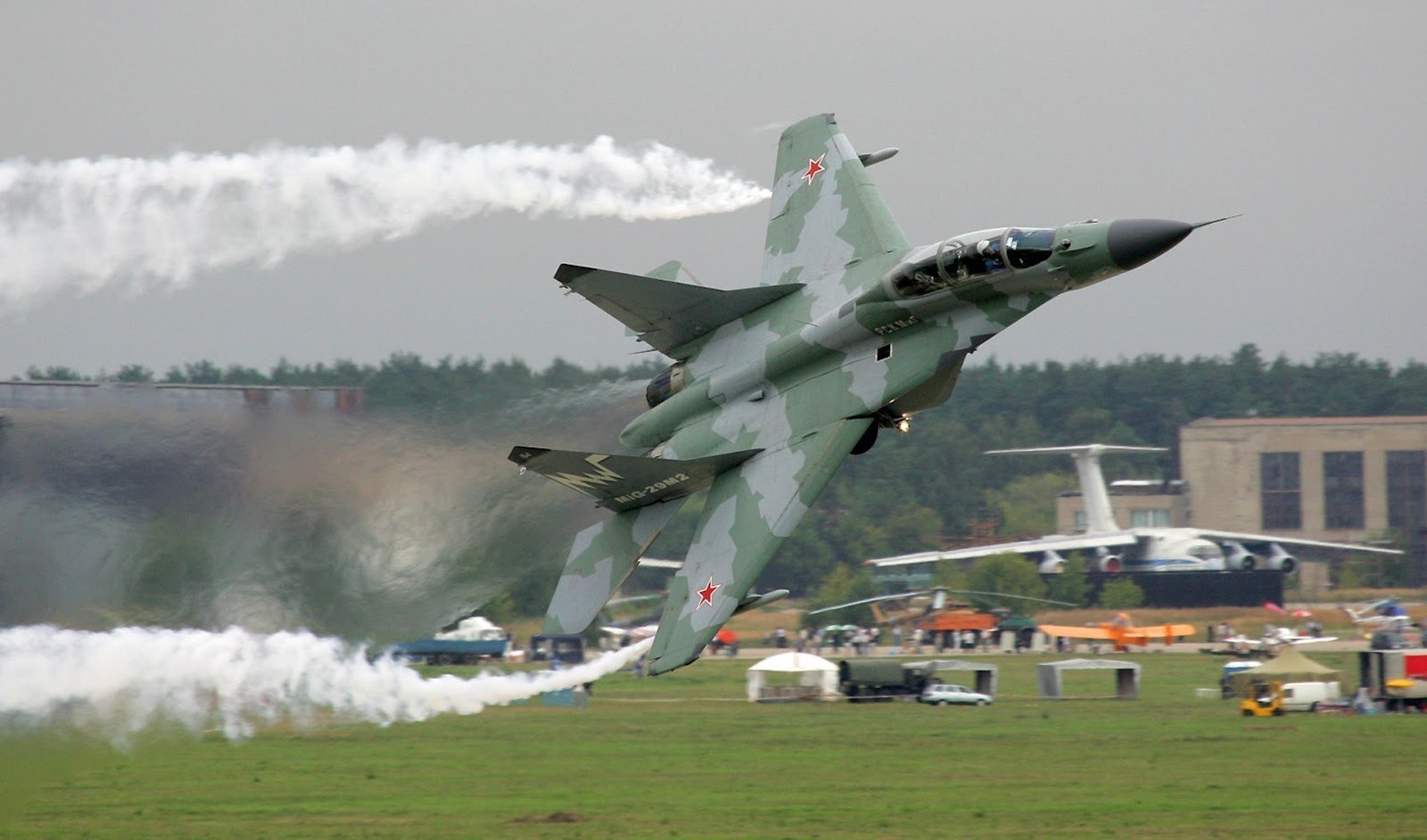 MiG-29 climbing steeply during a low demonstration pass with white smoke trails.
