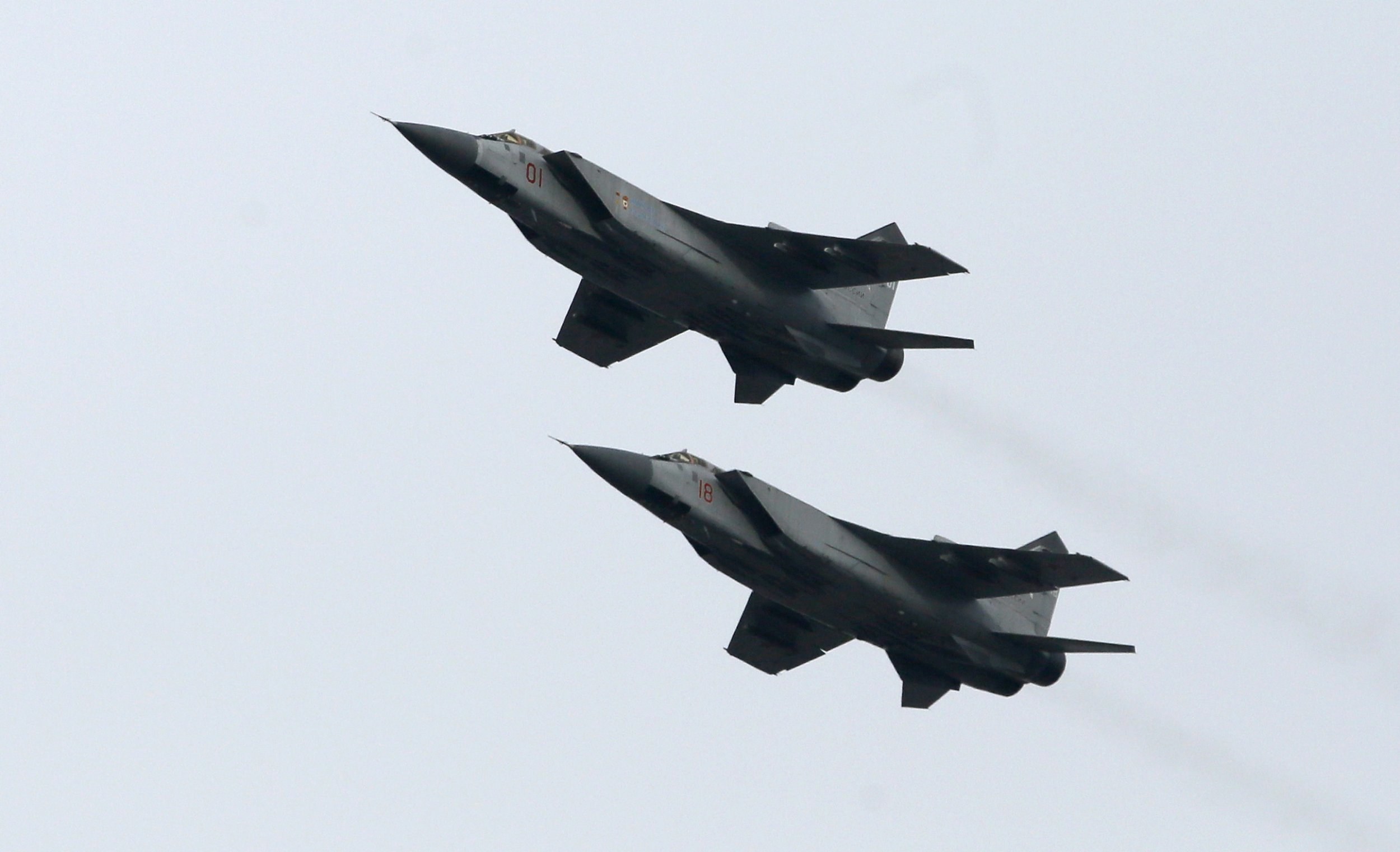 Two dark MiG-31 aircraft flying in formation against a pale sky.