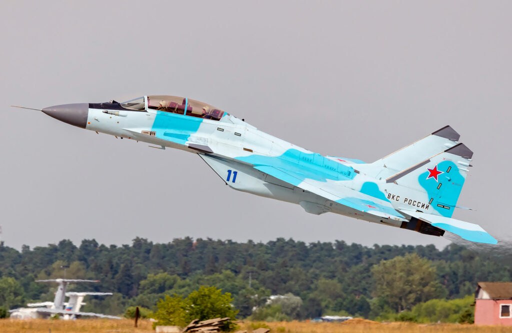 Light blue and gray MiG-35 numbered 11 climbing low with Russian markings.