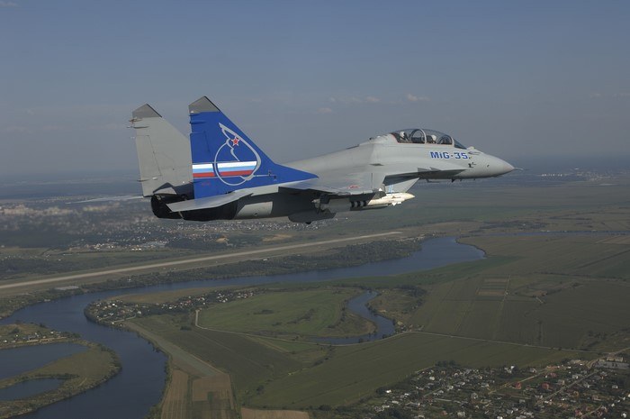 MiG-35 numbered 154 flying over rivers and fields with a blue tail design.