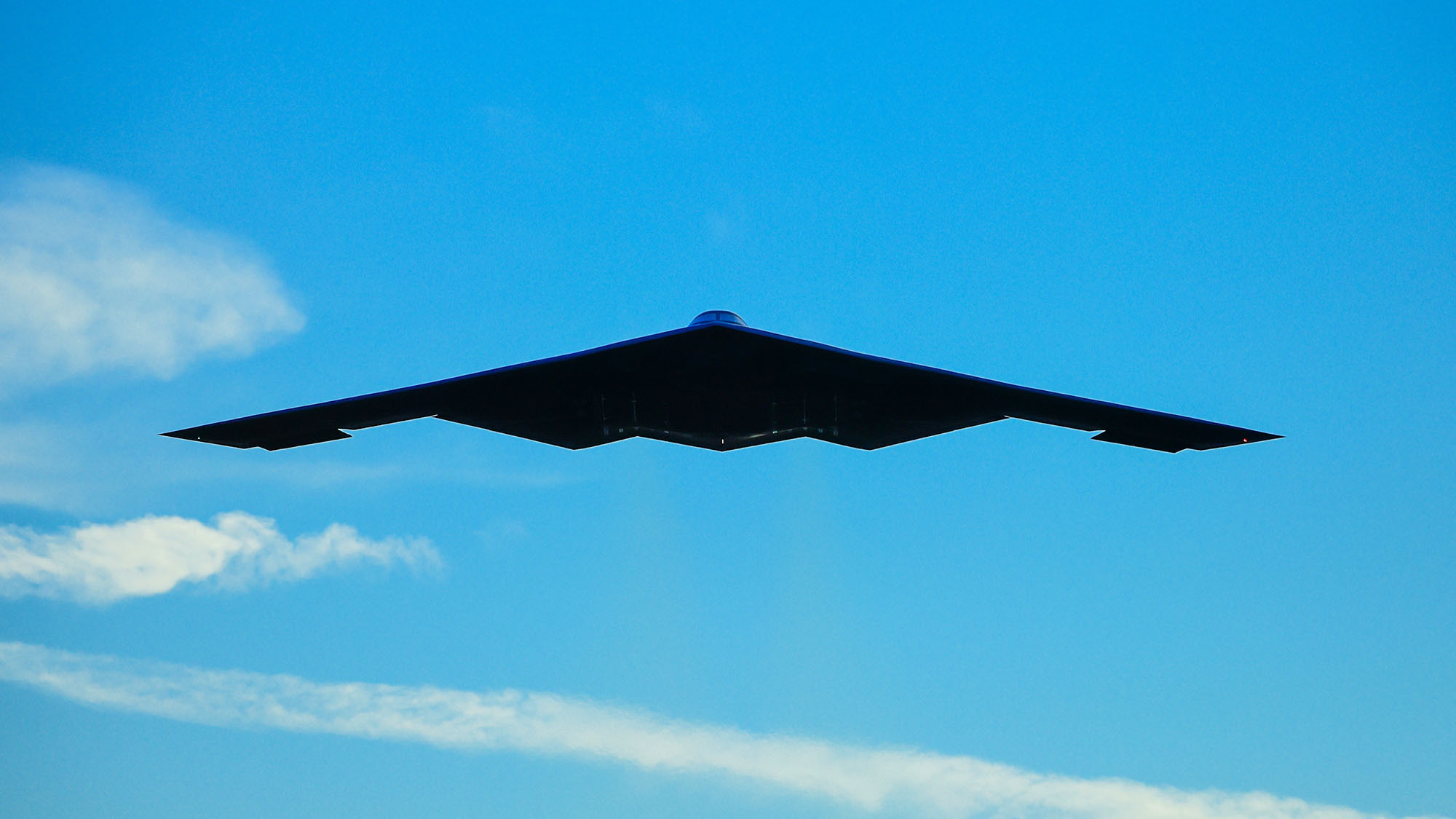 B-2 Spirit flying-wing aircraft silhouetted against blue sky