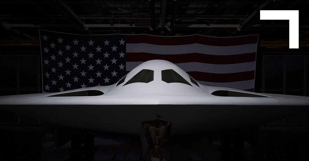 B-21 Raider front view inside a hangar with an American flag behind it