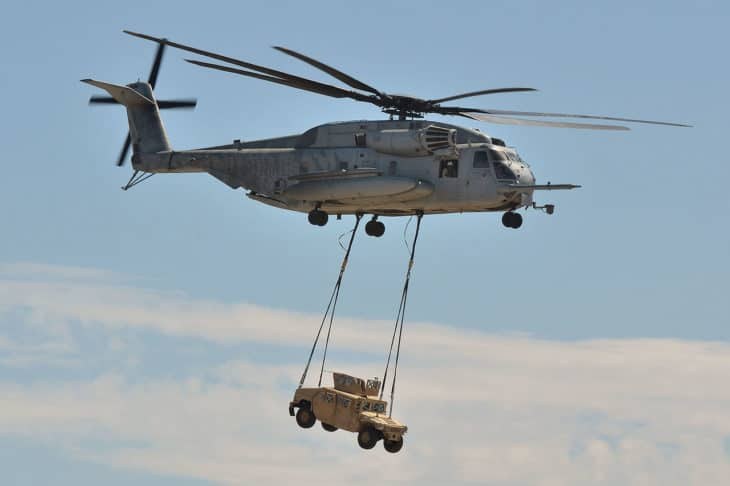 Sikorsky CH-53E Super Stallion flying with a small vehicle suspended below by cables.