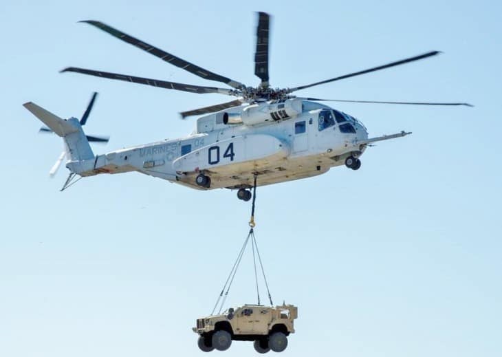 Sikorsky CH-53K King Stallion number 04 flying with a vehicle suspended underneath.