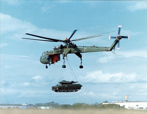 Sikorsky CH-54 Tarhe flying with a tracked vehicle suspended underneath.