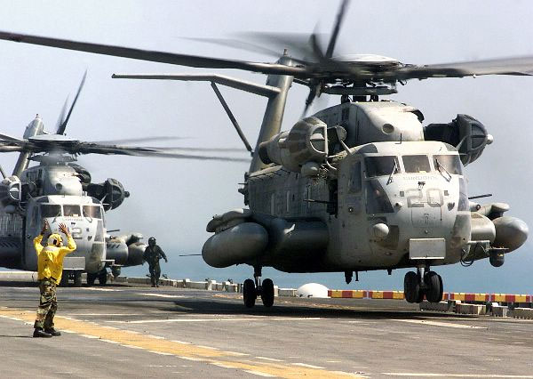 Sikorsky CH-53 Super Stallion on a ship deck with crew nearby, showing the heavy-lift helicopter in naval service context.