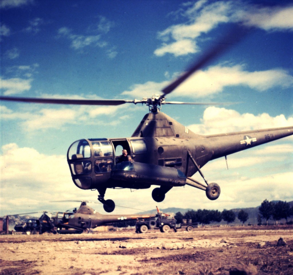 Sikorsky R-5 hovering over a rough field with U.S. marking visible.
