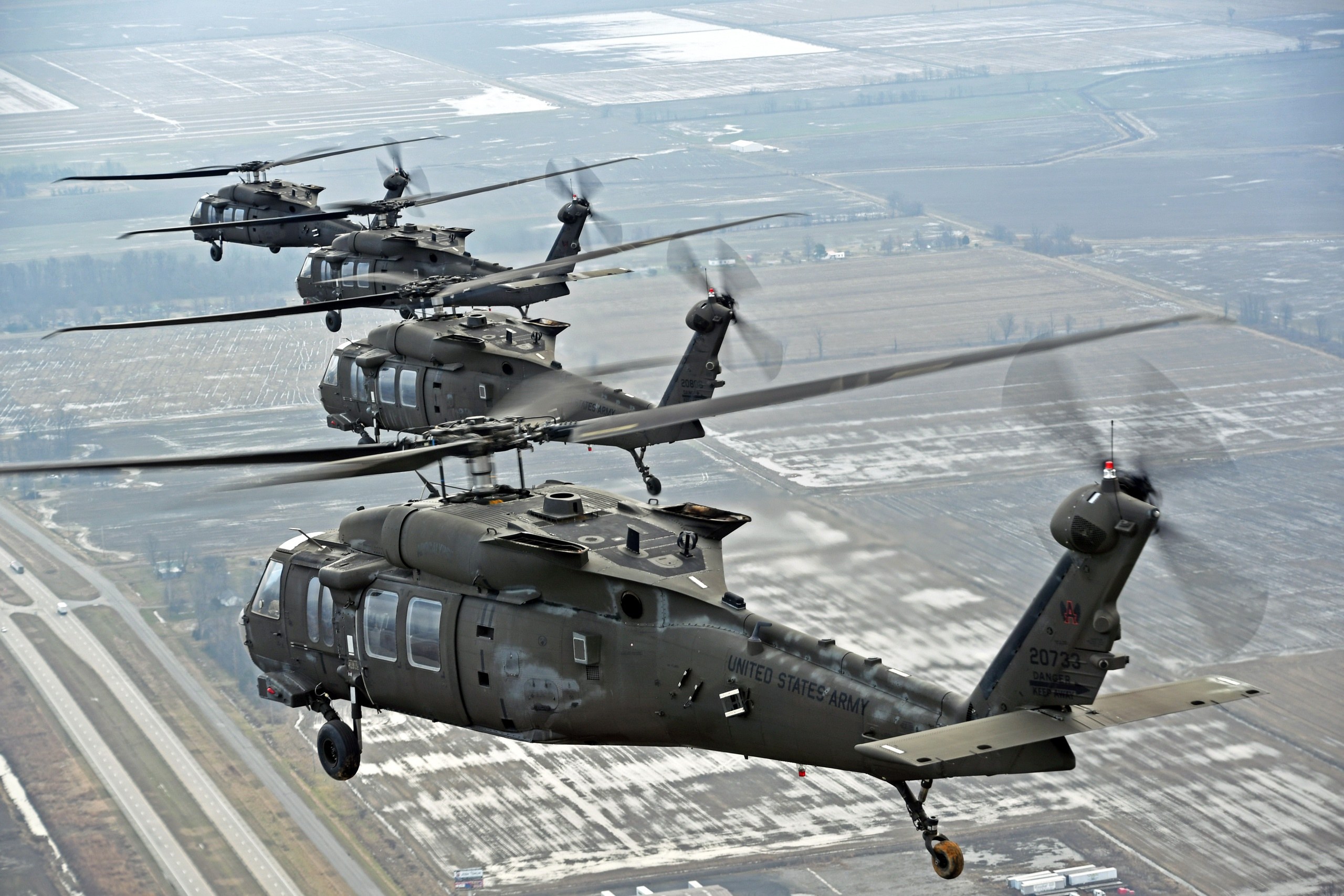 Four Sikorsky UH-60 Black Hawk helicopters flying in formation over an airfield.